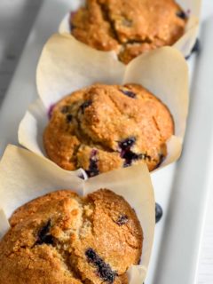three jumbo blueberry muffins in paper liners on a platter.
