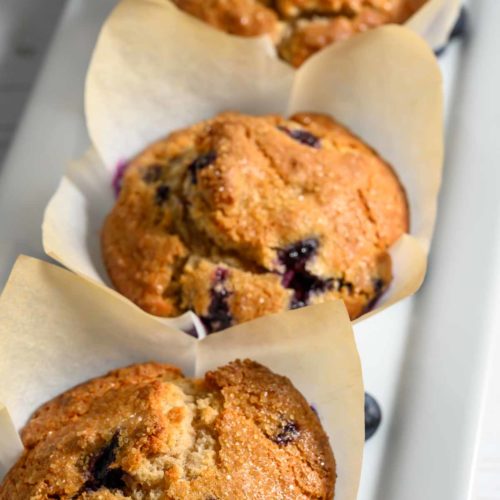 three jumbo blueberry muffins in paper liners on a platter.