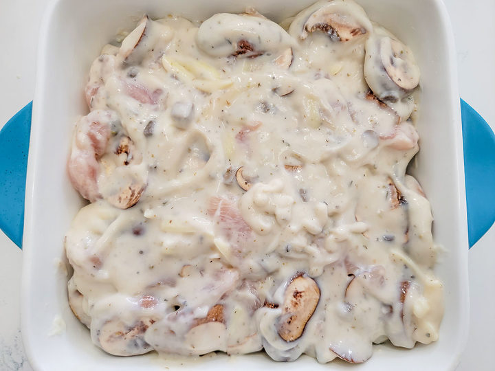pierogi, cheese, diced raw chicken, sliced mushrooms, chicken broth, cream of chicken soup, garlic powder, onion powder, Italian seasoning, and black pepper in a baking dish.