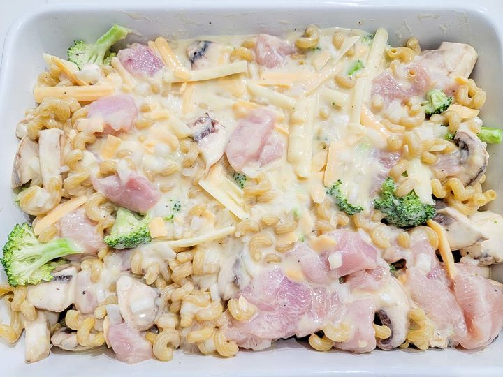 condensed soup, chicken broth, salt, pepper, garlic powder, onion powder, broccoli, raw chicken, and uncooked cavatappi pasta in a baking dish.