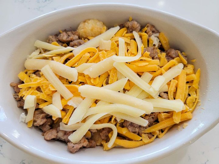 the tater tots, crumbled sausage, cheddar cheese, and mozzarella cheese in a baking dish..