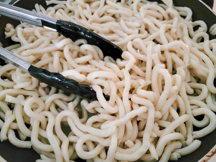 udon noodles cooking in a skillet.