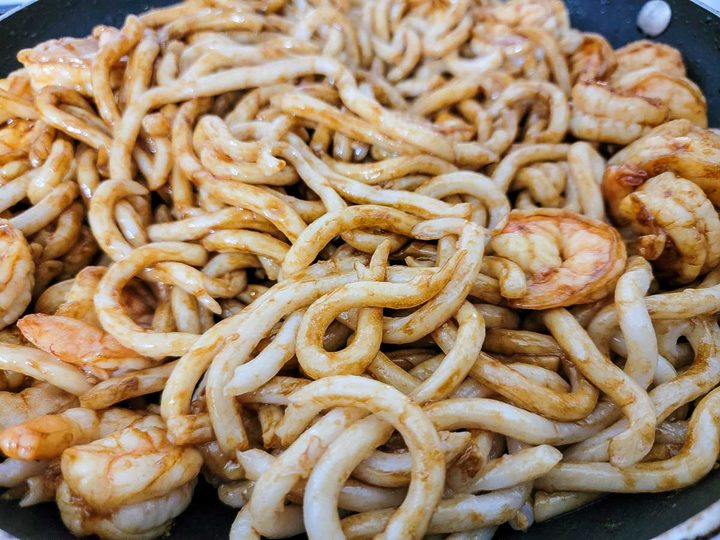 udon noodles and shrimp cooking in dark soy sauce.
