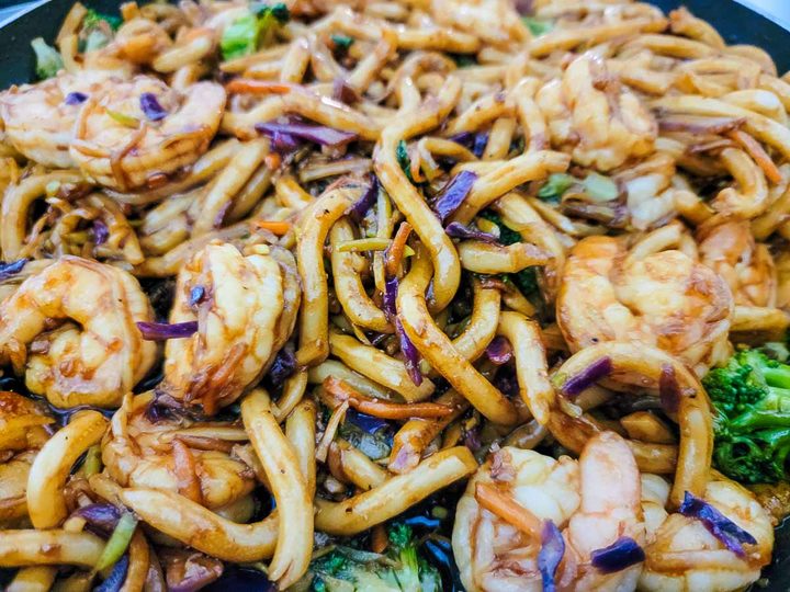broccoli slaw, udon noodles and shrimp cooking in dark soy sauce.