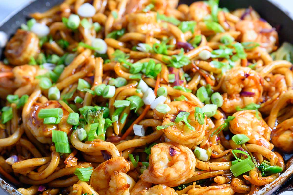 chewy udon noodles, tender shrimp, broccoli slaw, and stir fry sauce in a frying pan.