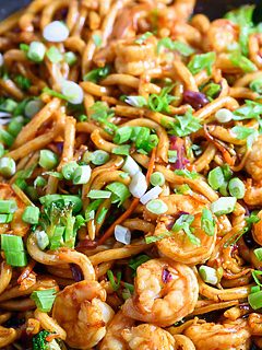 chewy udon noodles, tender shrimp, broccoli slaw, and stir fry sauce in a frying pan.