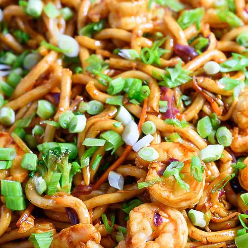 chewy udon noodles, tender shrimp, broccoli slaw, and stir fry sauce in a frying pan.