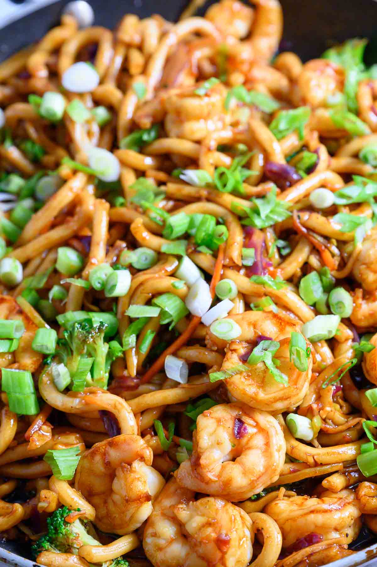 chewy udon noodles, tender shrimp, broccoli slaw, and stir fry sauce in a frying pan.