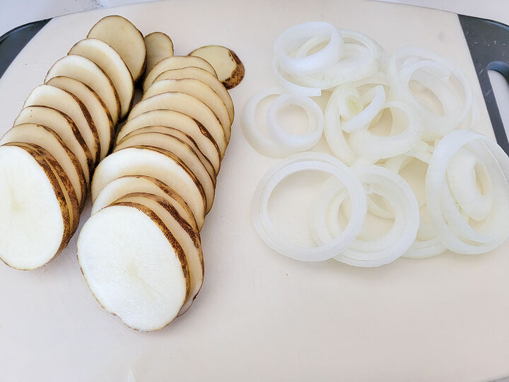 potato slices and onion slices on a cutting board.
