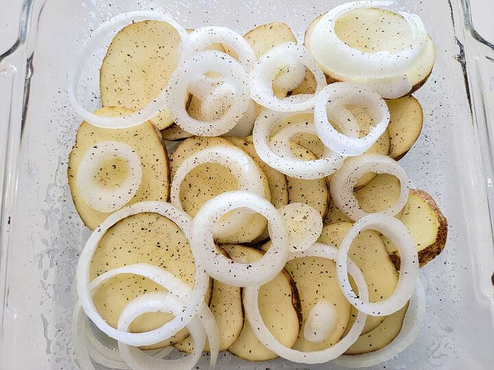 potato slices and onion slices topped with black pepper in a baking dish.