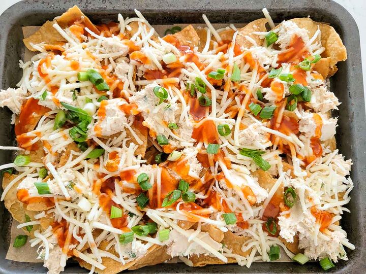 crab meat, cream cheese, green onion, Worcestershire sauce, soy sauce, and garlic powder, cheese, green onions, and sweet and sour sauce over tortilla chips on a baking sheet.