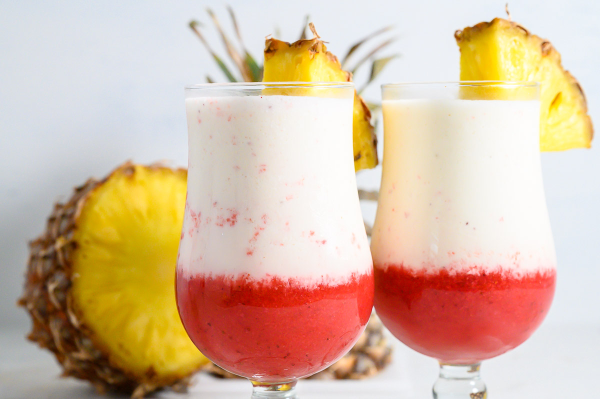 two Hawaiian Lava Flow Drinks garnished with pineapple wedges.