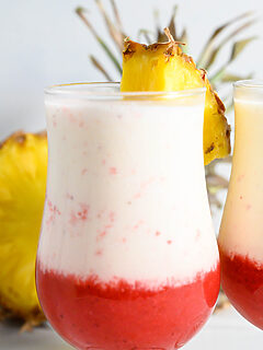 two Hawaiian Lava Flow Drinks garnished with pineapple wedges.