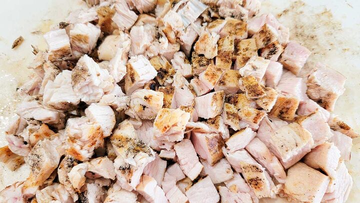 cooked chicken cubed on a cutting board.