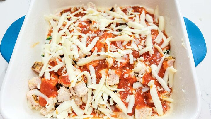 lasagna noodles layered with chicken, cheese, spaghetti sauce, cream cheese, and spinach in a baking dish.