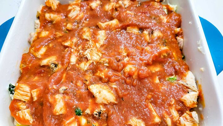 lasagna noodles layered with chicken, cheese, spaghetti sauce, cream cheese, and spinach in a baking dish.