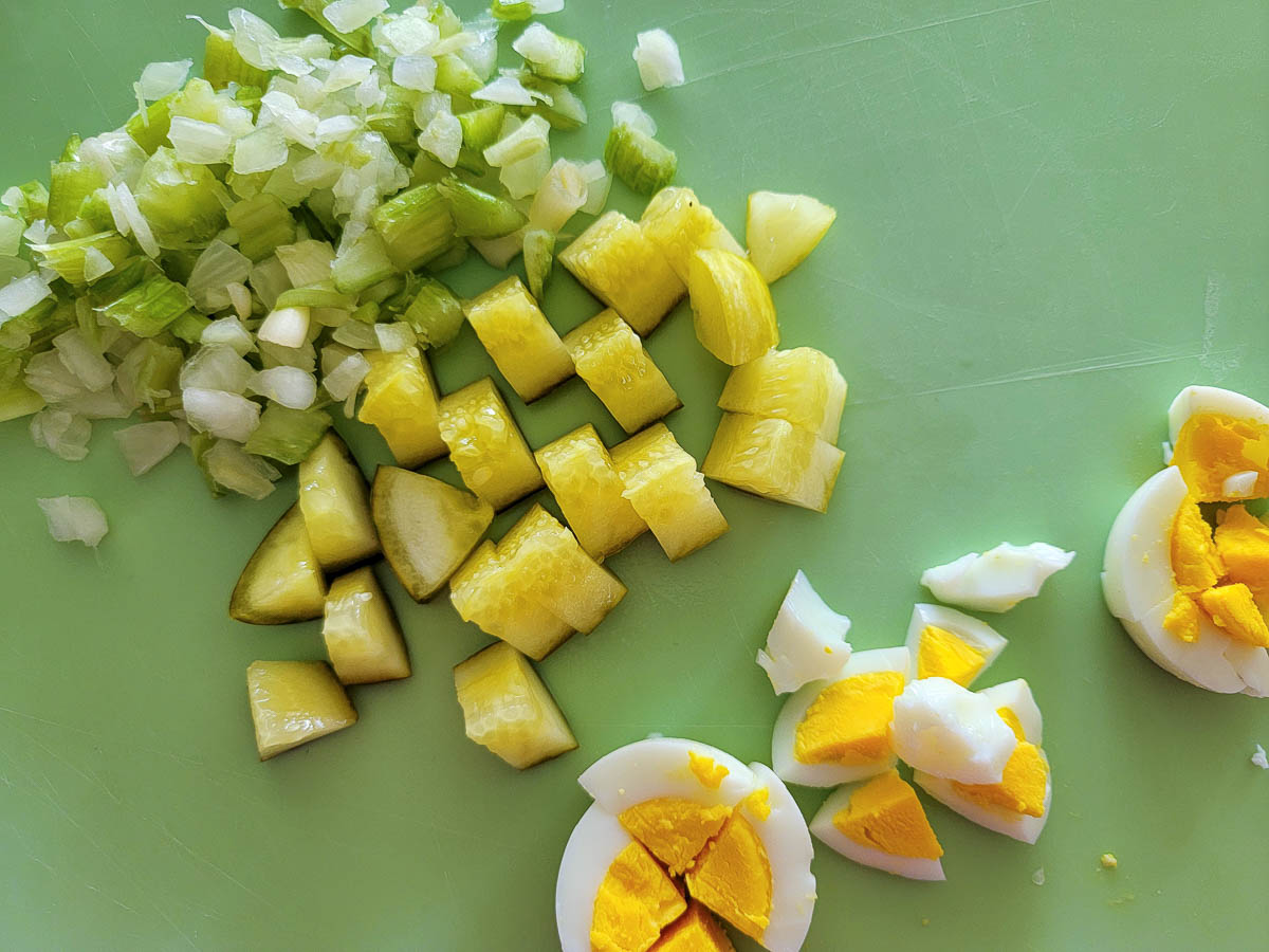 dice celery, onion, dill pickles, and hard-boiled eggs on a cutting board.