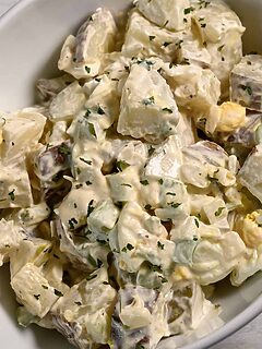 a bowl of Potato Salad loaded with bacon, tender potatoes, egg, diced dill pickles, onions, and celery smothered in a simple dressing of mayo, seasoned salt, and black pepper.