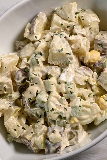 a bowl of Potato Salad loaded with bacon, tender potatoes, egg, diced dill pickles, onions, and celery smothered in a simple dressing of mayo, seasoned salt, and black pepper.