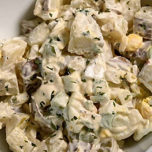 a bowl of Potato Salad loaded with bacon, tender potatoes, egg, diced dill pickles, onions, and celery smothered in a simple dressing of mayo, seasoned salt, and black pepper.