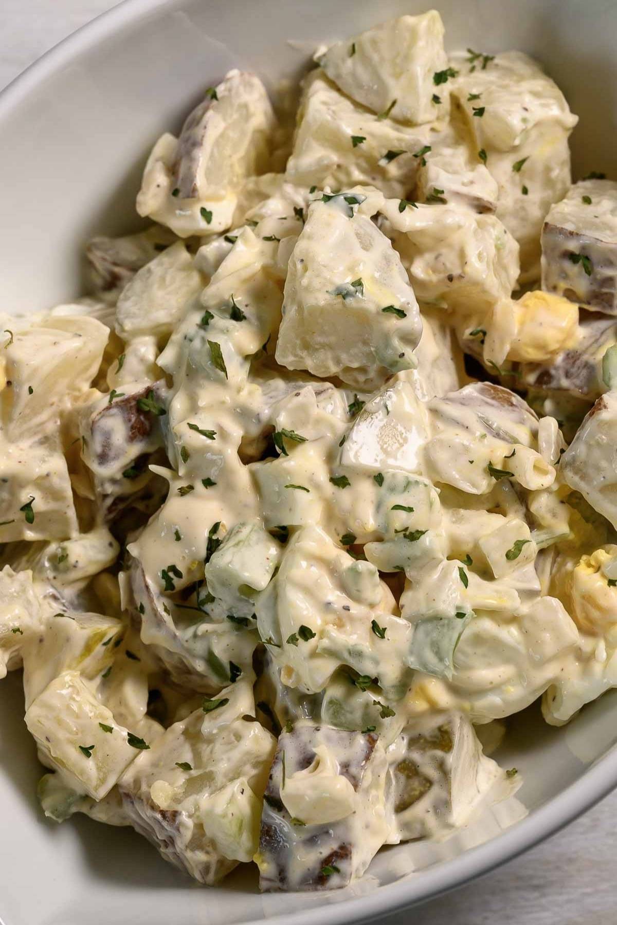 a bowl of Potato Salad loaded with bacon, tender potatoes, egg, diced dill pickles, onions, and celery smothered in a simple dressing of mayo, seasoned salt, and black pepper.