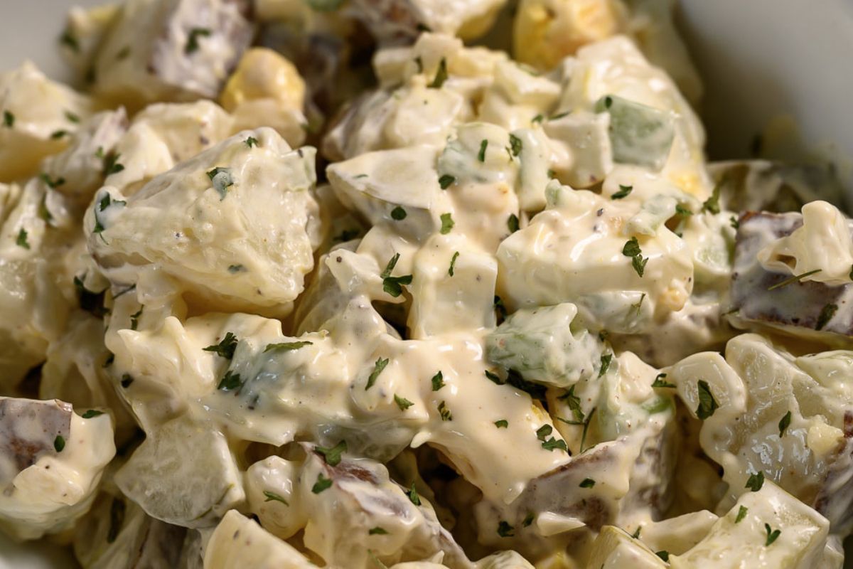 a bowl of Potato Salad loaded with bacon, tender potatoes, egg, diced dill pickles, onions, and celery smothered in a simple dressing of mayo, seasoned salt, and black pepper.