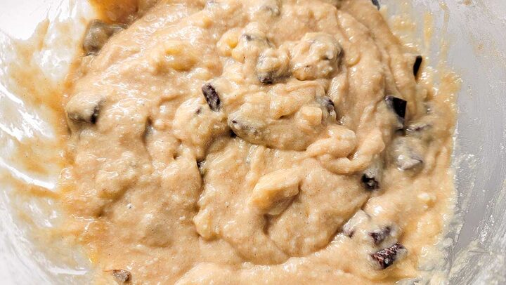 mashed banana, butter, sugar, eggs, vanilla, flour, baking soda, salt, and chocolate chunks mixed in a bowl.
