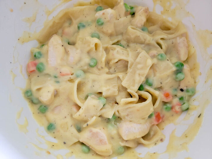 chicken, peas, carrots, thick egg noodles, and creamy sauce in a bowl.