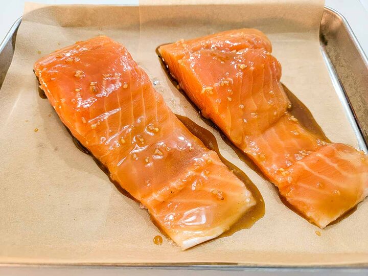 salmon filets topped with maple syrup glaze on a baking sheet.